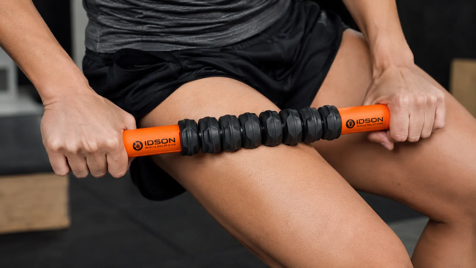 Close-up of hands gripping the Idson muscle roller stick handles while pressing it into a quad muscle
