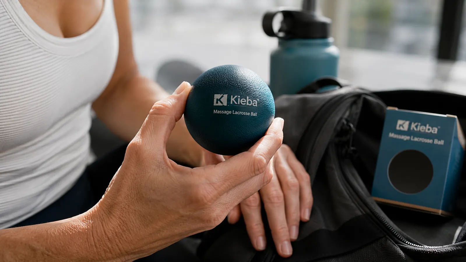 Close-up of a hand holding a Kieba lacrosse ball with a gym bag in the background