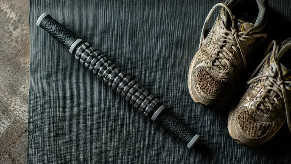 Muscle roller stick resting on a yoga mat next to a pair of running shoes
